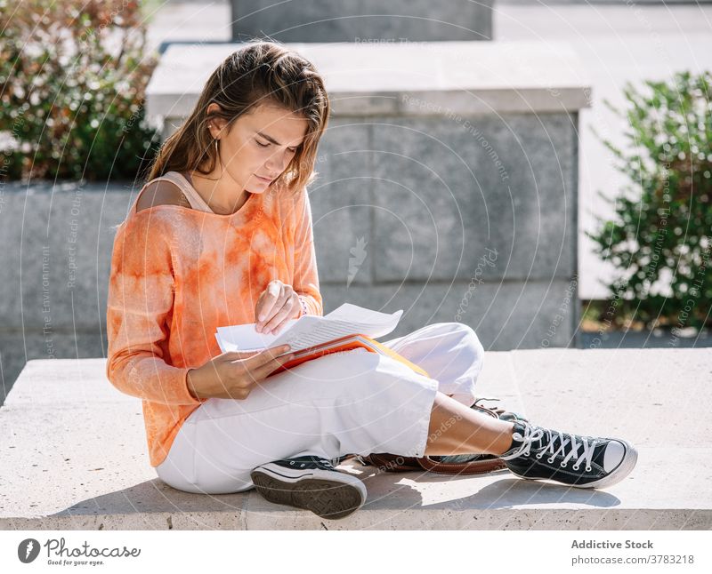 Junge Studentin sitzt an der Grenze und öffnet Notizbuch Frau Schüler Universität Notebook offen Hausaufgabe Borte sitzen Bildung Straße lernen lesen