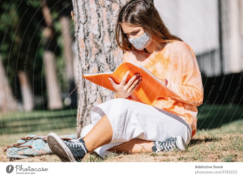 Studentin in Maske liest in der Nähe von Baum Frau Schüler Universität Notebook lesen Hausaufgabe Mundschutz Bildung Pandemie Straße lernen Prüfung vorbereiten