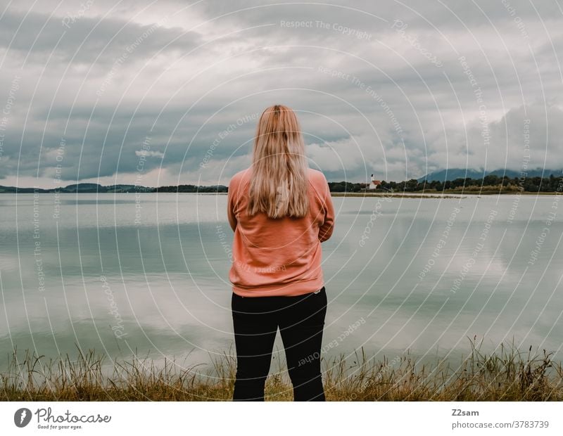 Junger Frau steht vor dem Forggensee in Füssen Junge Frau blond Rückansicht Erholung Pause Freiheit Sommer Sonne Reflexion & Spiegelung See Seeufer hübsch