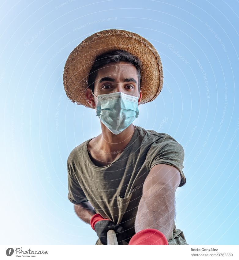Junger Mann als Bauer mit Schutzmaske in Zeiten von 19 Jahren und von unten gesehen jung Landwirt arbeiten Arbeiter Strohhut brünett brünettes Haar Handschuhe