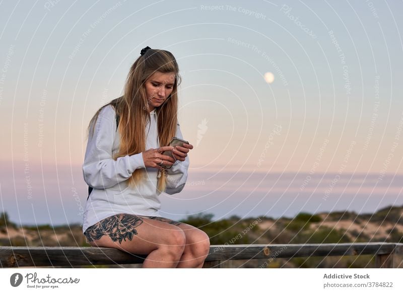 Friedliche Frau, die auf der Promenade bei Sonnenuntergang auf ihrem Smartphone surft Spazierweg reisen Browsen benutzend Dämmerung sich[Akk] entspannen