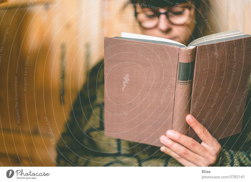 Eine frau mit Brille liest zuhause ein Buch lesen Leseratte gemütlich Lesestoff Roman Bildung Literatur vertieft konzentriert Pullover dunkelhaarig brünett