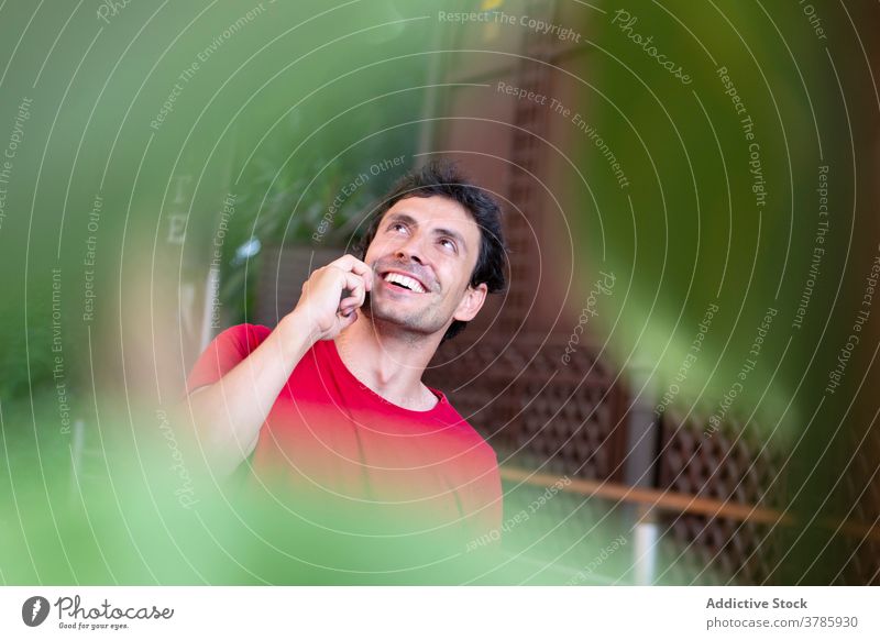 Positiver junger Mann mit rotem T-Shirt, der einen Anruf tätigt und lächelt Station Smartphone Lifestyle Sprechen Unternehmer Öffentlich urban Kaukasier modern