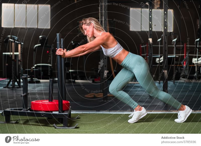 Muskulöse Frau schiebt Schlitten im Fitnessstudio schieben Gewicht Rodel Training schwer Gerät Übung stark muskulös Sportlerin passen Metall intensiv Wellness