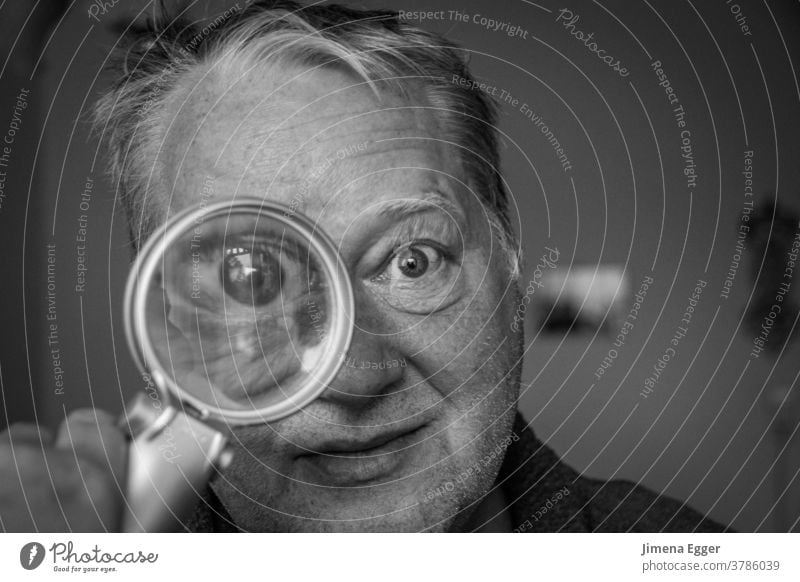 älterer Mann schaut durch Lupe vergrößert Auge Blick Linse Glas untersuchen Suche Mensch Detektiv Neugier beobachten Porträt Blick in die Kamera Gesicht