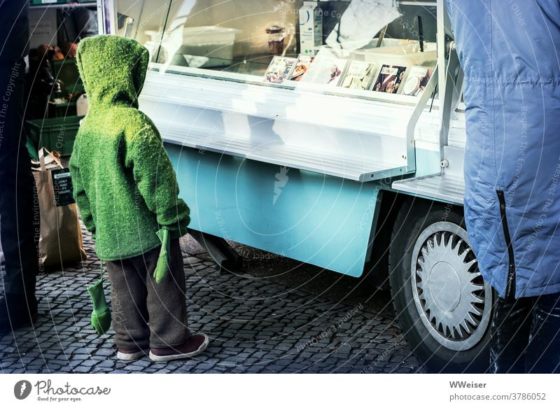 Winterlich angezogenes Kind schmachtet das Angebot des Eiswagens an Strickjacke Kapuze Fäustlinge Handschuhe Vitrine Auslage Verkaufsstand Marktstand