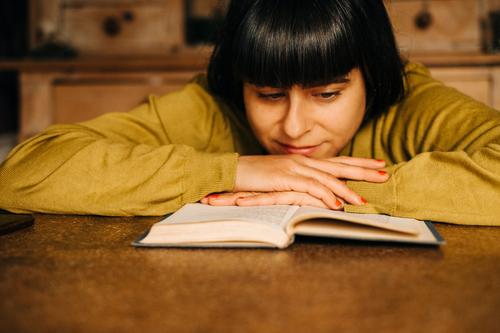 Eine Frau sitzt zuhause am Küchentisch und liest ein Buch lesen Leseratte gemütlich Lesestoff Roman Bildung Literatur vertieft konzentriert Pullover