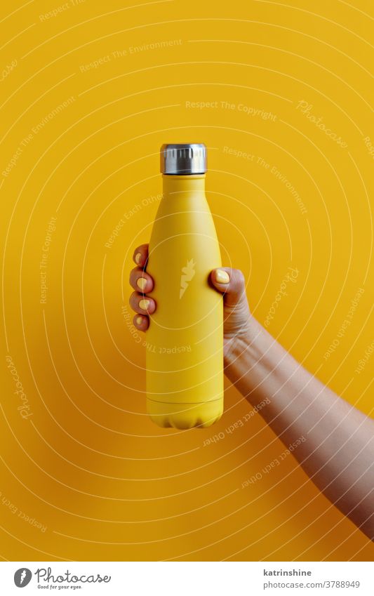 Nahaufnahme einer weiblichen Hand, die eine gelbe wiederverwendbare Stahlflasche auf gelbem Hintergrund hält Flasche Monochrom ökologisch Wasser Thermo hell