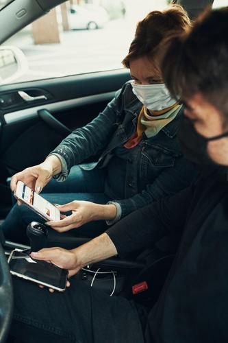 Mann und Frau sitzen in einem Auto und benutzen Smartphones und tragen die Gesichtsmasken, um eine Virusinfektion zu vermeiden Kaukasier covid-19 Lifestyle