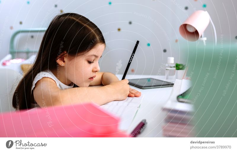 Mädchen macht Hausaufgaben am Schreibtisch sitzend schreibend Homeschooling Schule zu Hause ruhig falsche Bleistifthaltung heimwärts Nahaufnahme Schlafzimmer