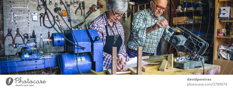 Seniorenpaar in einer Tischlerei Zimmerer Gehrung benutzend Schreinerei Paar arbeiten Blick plant Werkstatt Transparente Panorama panoramisch Netz Holz reif