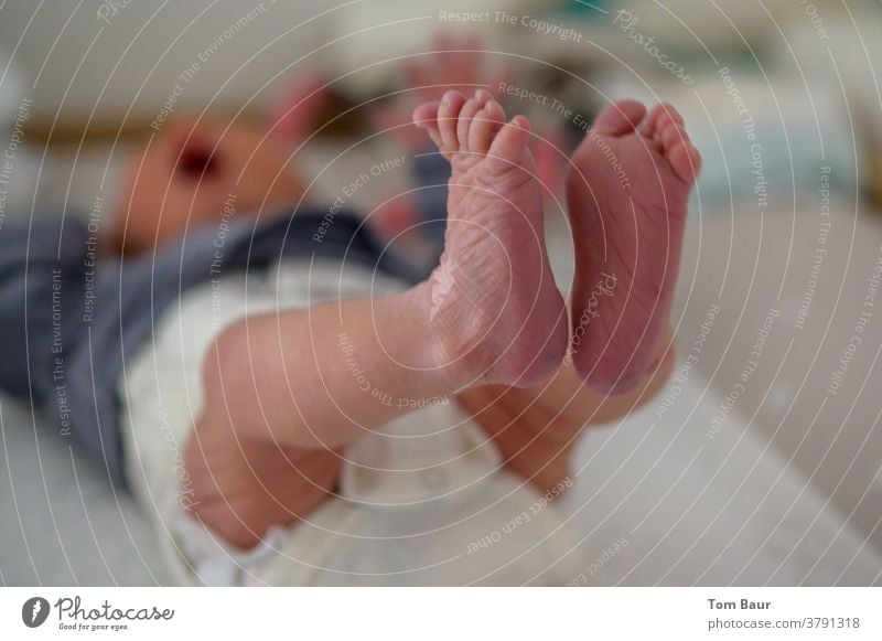 Nahaufnahme der Füße des Babys, während das Baby auf dem Wickeltisch liegt und seine Füßchen in die Luft streckt im verschwommenen Hintergrund sieht man, dass das Baby weint
