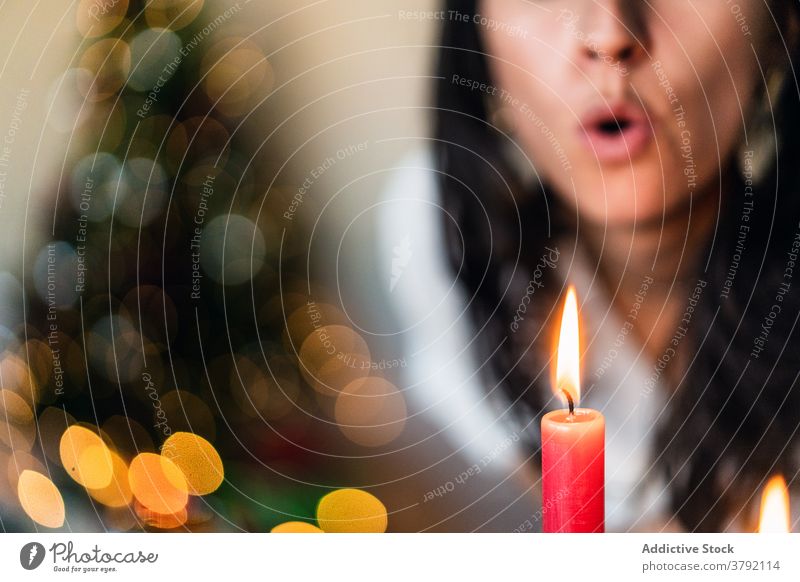 Crop Frau bläst auf glühende Kerze Flamme während festlichen Veranstaltung Schlag Feuer Brandwunde Weihnachten Dekoration & Verzierung Mund geöffnet farbenfroh