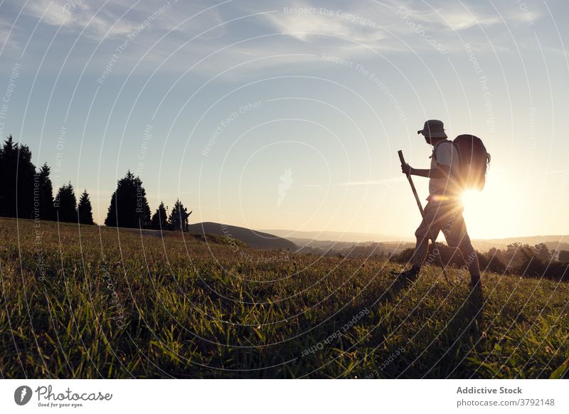 Anonymer Wanderer mit Rucksack und Stock, der auf einem Grashügel geht Spaziergang Pilger Sonnenschein reisen Trekking kleben wolkig Himmel Tourist Abend