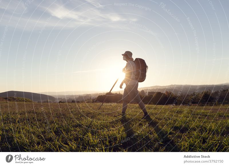 Anonymer Wanderer mit Rucksack und Stock, der auf einem Grashügel geht Spaziergang Pilger Sonnenschein reisen Trekking kleben wolkig Himmel Tourist Abend