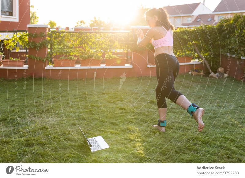 Schlanke Frau macht Übungen im Innenhof im Sommer Training Laptop online Tutorial benutzend Athlet Sonnenuntergang Sportbekleidung Gesundheit Fitness Internet
