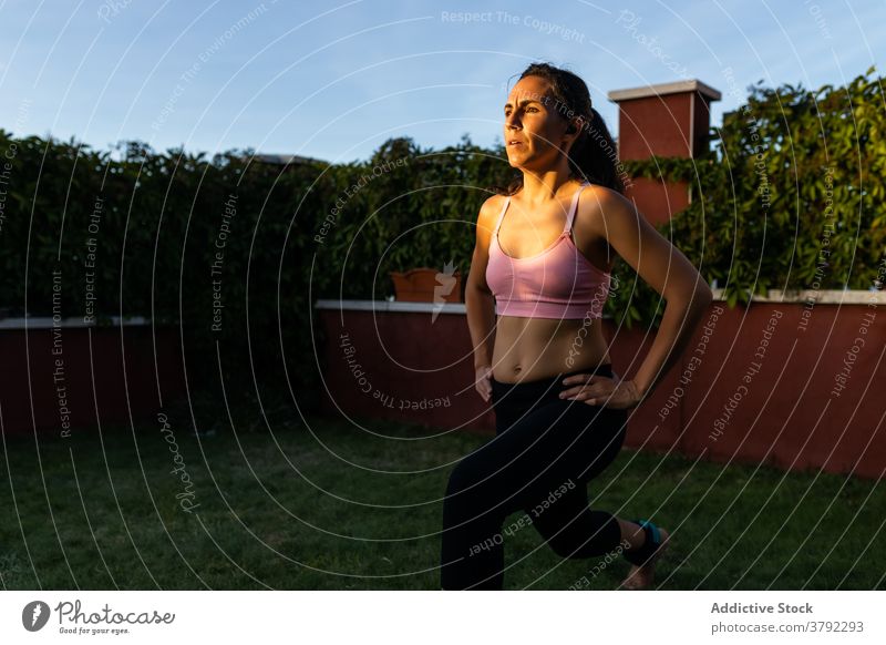 Schlanke Frau macht Übungen im Innenhof im Sommer Ausfallschritt Training Laptop online Tutorial benutzend Athlet Sonnenuntergang Sportbekleidung Gesundheit