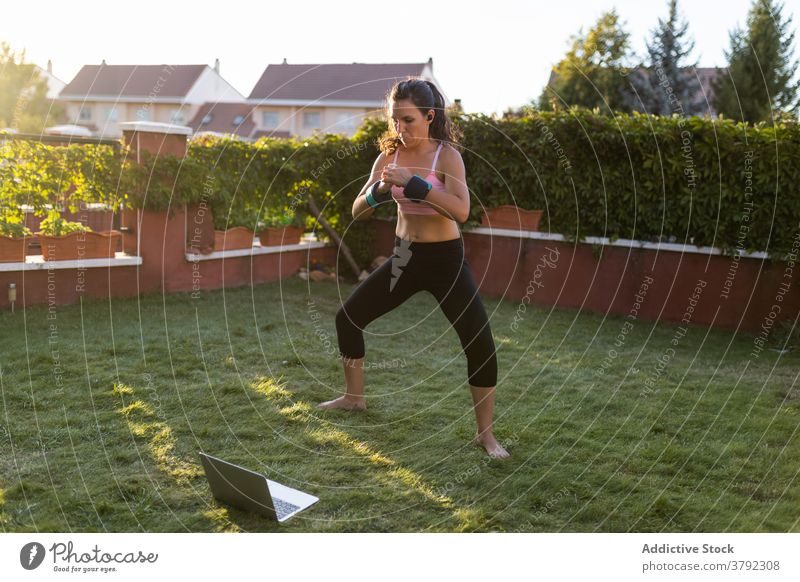 Schlanke Frau macht Übungen im Innenhof im Sommer Training Kniebeuge Laptop online Tutorial benutzend Athlet Sonnenuntergang Sportbekleidung Gesundheit Fitness