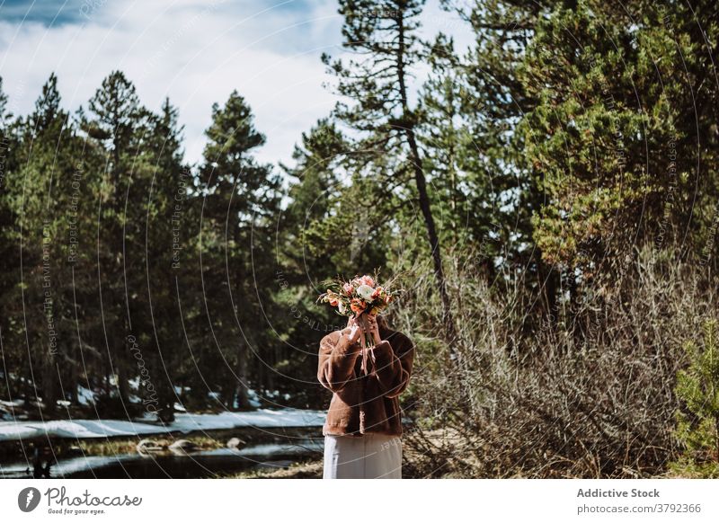 Unerkennbare Frau hält Blumenstrauß gegen Gesicht im Frühling Wald Tierhaut Deckblatt Natur Verkleidung Blütezeit warme Kleidung romantisch ruhig Windstille