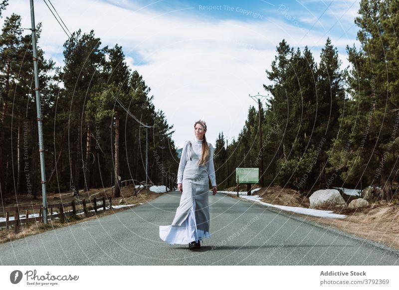 Ruhige Frau zu Fuß entlang der Straße in Nadelwald im Frühjahr Gelassenheit Spaziergang Route Spazierweg charmant Kleid Umwelt Wald schlendern Natur traumhaft