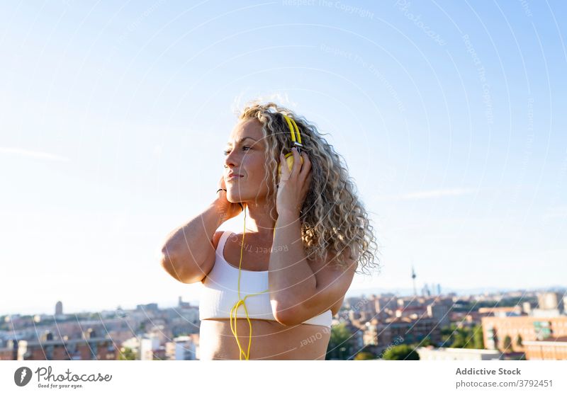 Positive Frau im Sport-BH hört Musik über Kopfhörer positiv optimistisch zuhören genießen Klang unterhalten Apparatur heiter sonnig Sommer jung Melodie Gesang