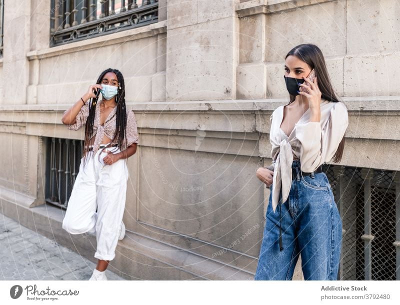 Stylish diverse Frauen in Masken sprechen auf Smartphones in der Stadt Zusammensein Straße Mundschutz Stil behüten Coronavirus Bund 19 vielfältig multiethnisch