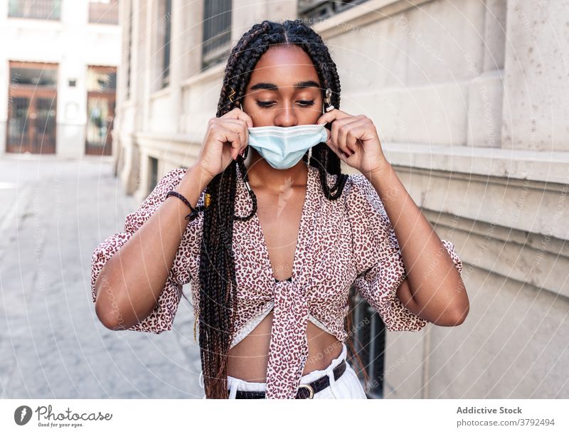 Stilvolle ethnische Frau in medizinischen Maske auf der Straße Mundschutz angezogen ausrichten Großstadt Ausbruch Bund 19 schwarz Afroamerikaner Geflecht Frisur