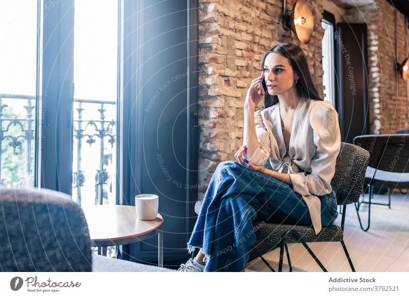 Frau trinkt Kaffee in der Nähe des Fensters, während sie ihr Smartphone benutzt trinken Stil brünett Gelassenheit sich[Akk] entspannen Mode Kälte ruhen elegant