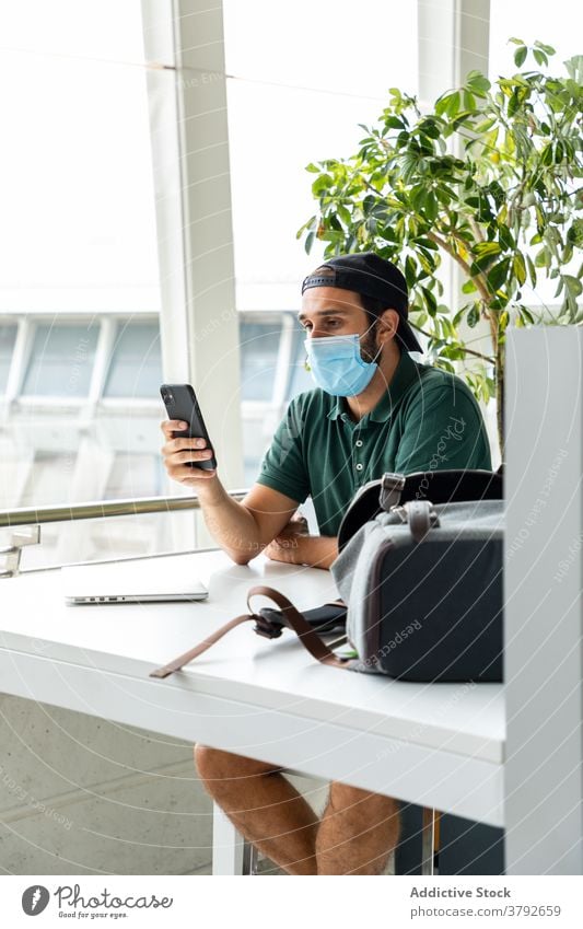 Mann mit Schutzmaske verwendet Smartphone Mundschutz medizinisch Coronavirus verhindern benutzend Lächeln männlich Laptop Foto Tisch heiter sitzen Glück Telefon