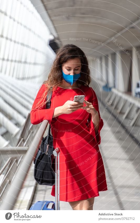 Reisende Frau mit Koffer im Flughafen Tourist Mundschutz Coronavirus Gepäck Smartphone benutzend Saal Abheben Pandemie reisen Ausflug Gerät warten Apparatur