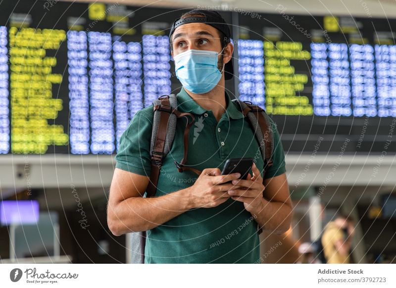 Reisender in Maske mit Handy im Flughafen warten Mann Abheben Terminal Holzplatte Smartphone benutzend Mundschutz männlich Bund 19 Passagier modern Browsen