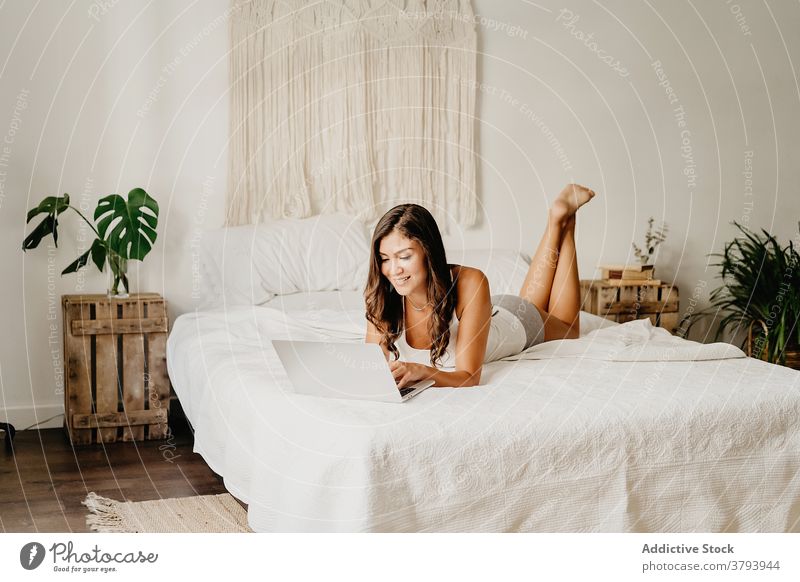 Fröhliche Frau, die auf dem Bett im Laptop surft Morgen benutzend Browsen Glück Schlafzimmer heimwärts heiter jung Gerät Apparatur Internet gemütlich sorgenfrei