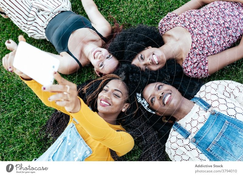 Entzückte multiethnische Freundinnen nehmen Selfie auf Gras Frauen Zusammensein Unternehmen Freundschaft Smartphone Selbstportrait heiter Spaß haben