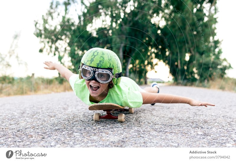Positives Kind auf Skateboard in Schutzbrille und dekorativem Helm Junge Spaß haben Brille Schutzhelm sorgenfrei genießen Mund geöffnet Aktivität Straße