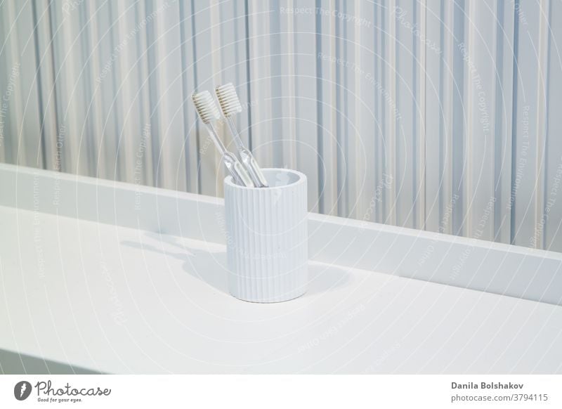 zwei Zahnbürsten in weißer, weißer Tasse im Badezimmer auf gestreiftem Hintergrund zahnärztliche Ausrüstung täglich Zahnbürstenhalter Karies Routine Reichtum