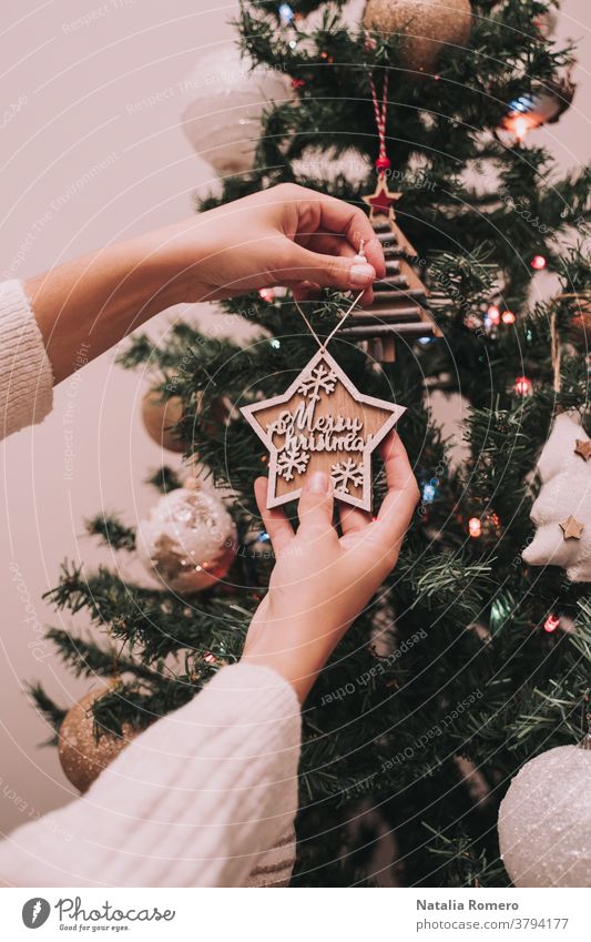 Eine Person schmückt den Weihnachtsbaum. Die Person hängt einen Weihnachtsstern mit einem Weihnachtsgruß auf. Nahaufnahme. Weihnachten dekorativ Feier