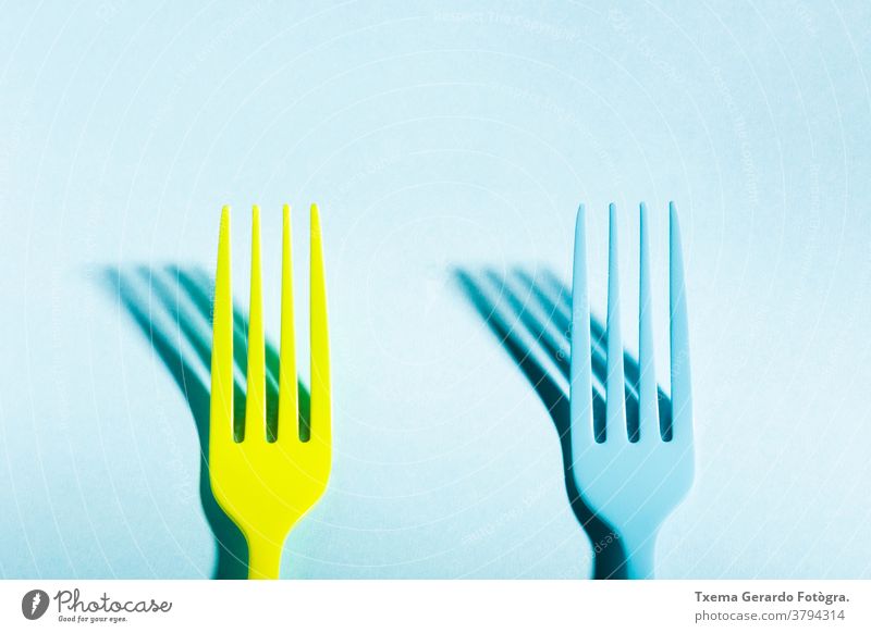 Zwei gelbe und blaue Gabeln werfen einen Schatten auf blauen Hintergrund gesättigt Farbe vereinzelt surreal Konzept Besteck Silberwaren Lebensmittel Draufsicht