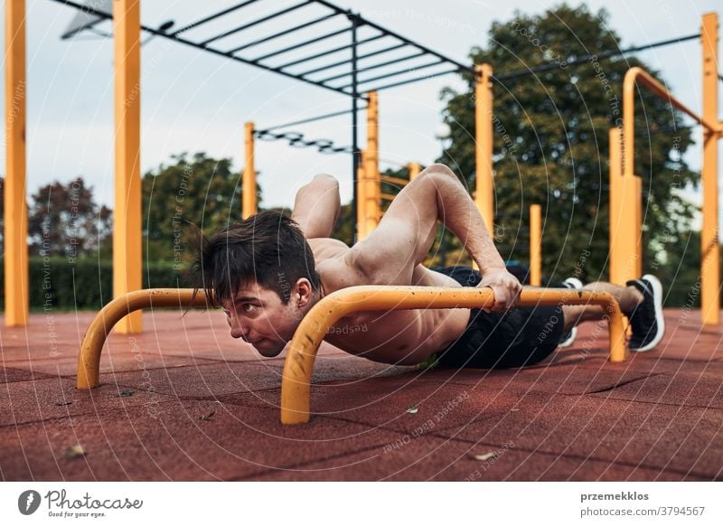 Junger Bodybuilder ohne Hemd, der während seines Trainings in einem modernen Gymnastikpark Liegestütze an einer parallelen Stange macht calisthenics Pflege