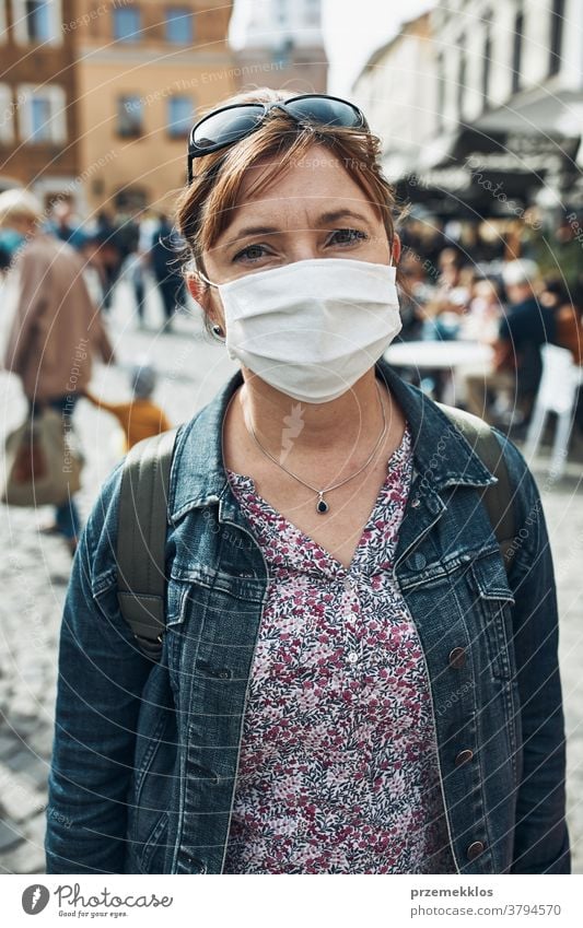 Junge Frau, die auf einer Straße in der Innenstadt steht und in die Kamera schaut, trägt die Gesichtsmaske, um eine Virusinfektion zu vermeiden Pflege Kaukasier