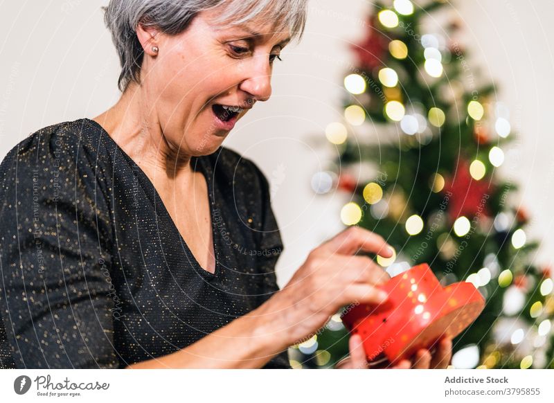 Überrascht Frau erhält Geschenk in Box in der Nähe von Weihnachtsbaum Überraschung Weihnachten präsentieren aufgeregt Kasten feiern heimwärts Feiertag elegant