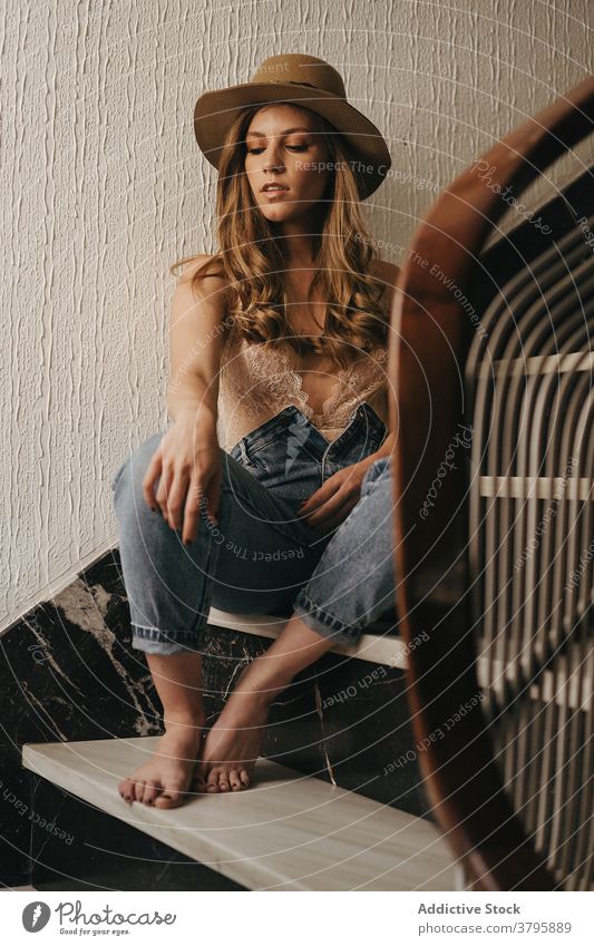 Stilvolle Frau sitzt auf der Treppe im Haus lässig Hut Jeanshose Vorschein Outfit charmant sich[Akk] entspannen Treppenhaus hölzern modern Schritt Urlaub ruhig