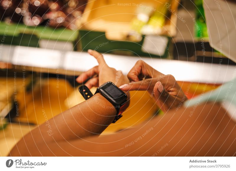 Ethnische Frau mit Schutzmaske überprüft Smartwatch im Supermarkt Mundschutz Coronavirus intelligente Uhr prüfen benutzend Kunde COVID behüten Käufer