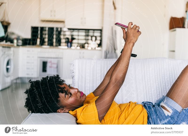 Lachende schwarze Frau nimmt Selfie mit Smartphone zu Hause benutzend heimwärts Spaß haben aufgeregt Browsen Mobile heiter tausendjährig jung Jugendlicher