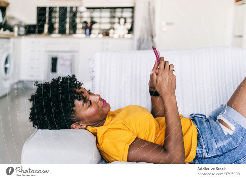 Lachende schwarze Frau, die ein Smartphone zu Hause benutzt benutzend heimwärts Spaß haben aufgeregt Browsen Mobile heiter tausendjährig jung Jugendlicher