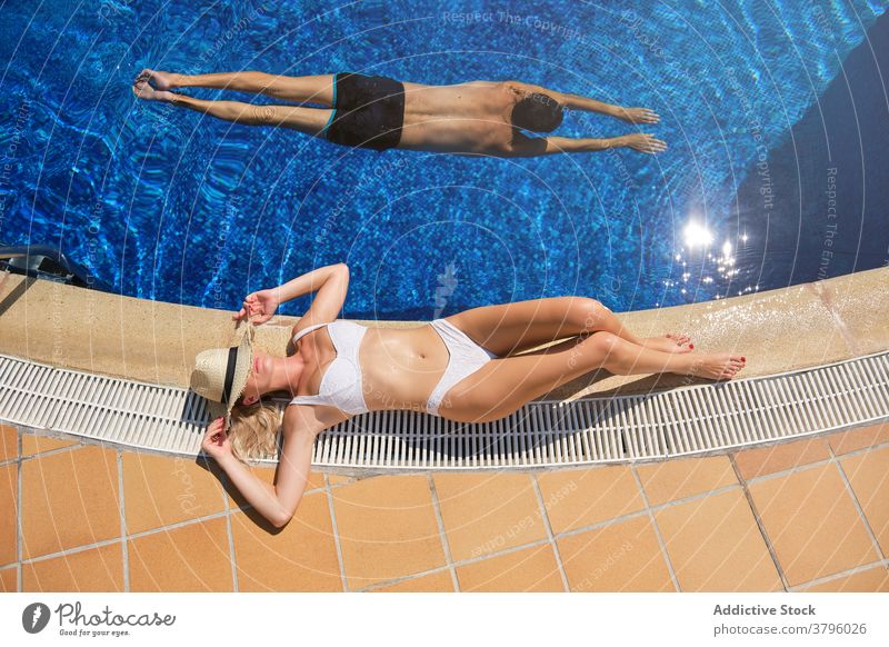 Junge Frau beim Sonnenbaden am Pool in einem Resort Lügen Beckenrand sich[Akk] entspannen Sommer Feiertag Stil reisen Bräune jung schlank Bikini Strohhut