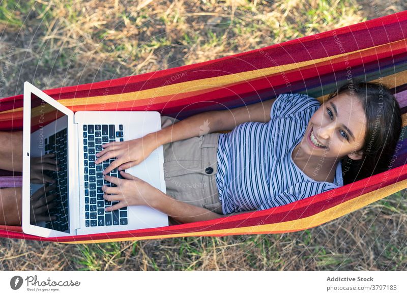 Lächelnde Frau in Hängematte mit Laptop freiberuflich Projekt benutzend Tippen Inbetriebnahme unabhängig heiter jung Internet Apparatur Gerät Netbook Browsen