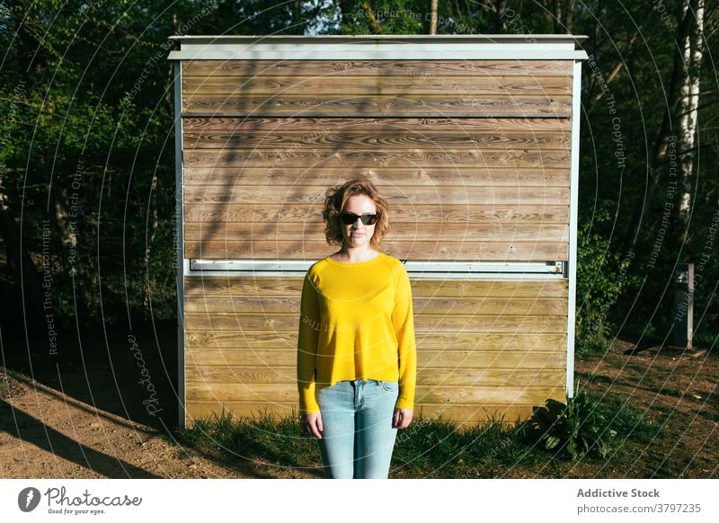 Stilvolle Frau in gelbem Outfit im Park trendy Mode Sonnenlicht Farbe lebhaft Sonnenbrille Inhalt Lächeln hölzern Gebäude sich[Akk] entspannen modern stehen