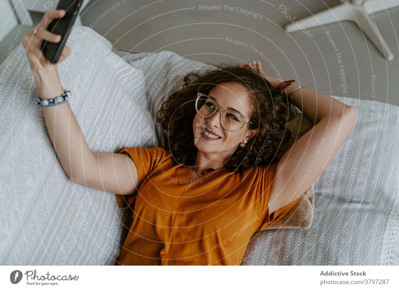 Junge Frau nimmt Selbstporträt auf Smartphone liegend auf Sofa Selfie Lügen sich[Akk] entspannen soziale Netzwerke Komfort benutzend Apparatur heimwärts Gerät