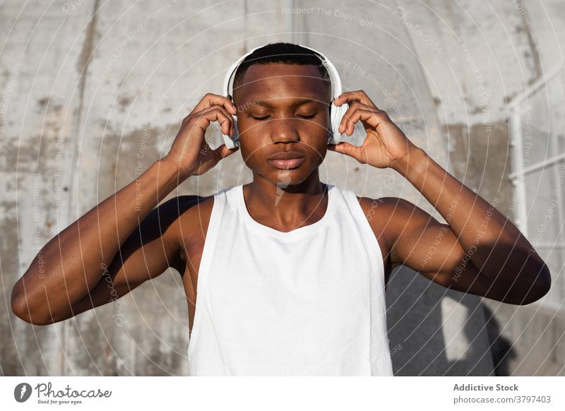 Schwarzer ernster Mann, der mit Kopfhörern Musik hört Windstille Augen geschlossen sich[Akk] entspannen Gesang Athlet zuhören Drahtlos Klang männlich ruhen