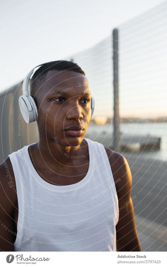 Schwarzer Sportler mit Kopfhörern beim Ausruhen nach dem Training Mann Athlet ernst muskulös sportlich Musik zuhören passen männlich Sportbekleidung Lifestyle
